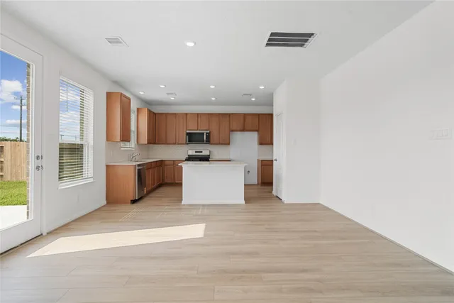 a large kitchen with stainless steel appliances granite countertop a stove a sink a refrigerator and white cabinets with wooden floor