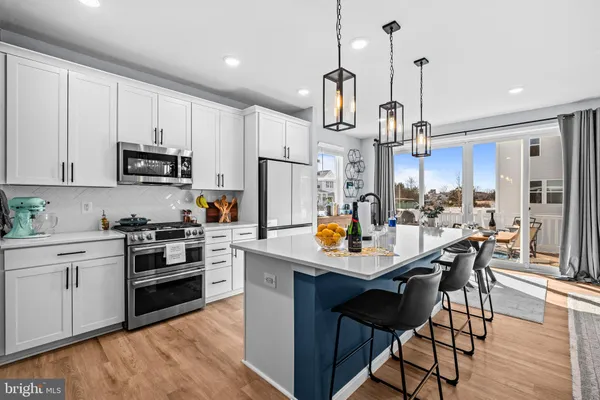 a kitchen with stainless steel appliances kitchen island granite countertop a sink a stove a refrigerator and white cabinets with wooden floor