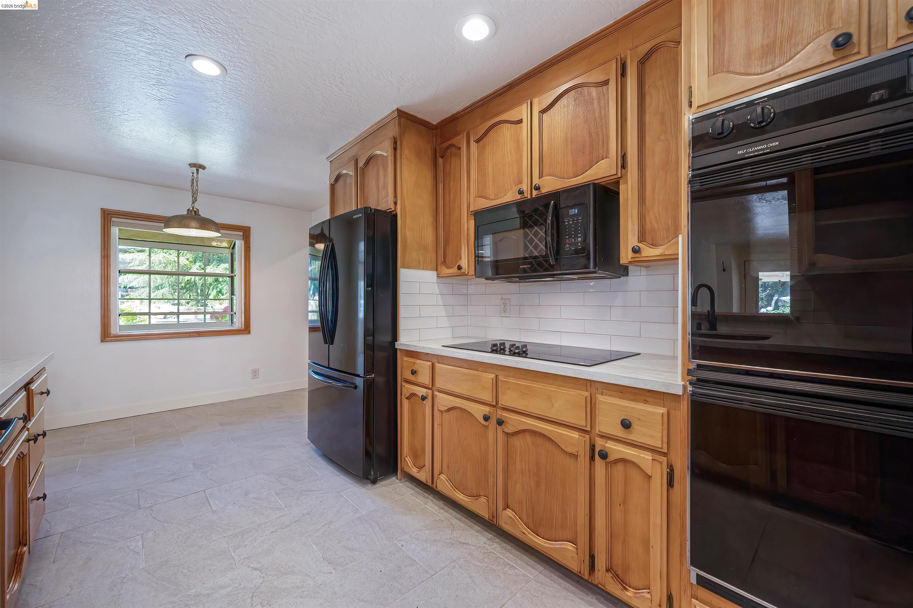 10474 Sheldon Road Elk Grove, CA 95624 - Photo 22 of 83 Kitchen featuring natural wood cabinetry, white subway tile backsplash, light-toned countertops, and integrated black appliances