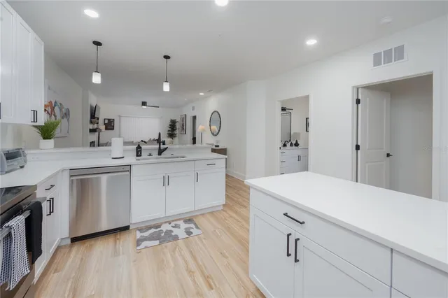 a kitchen with a sink dishwasher and white cabinets with wooden floor