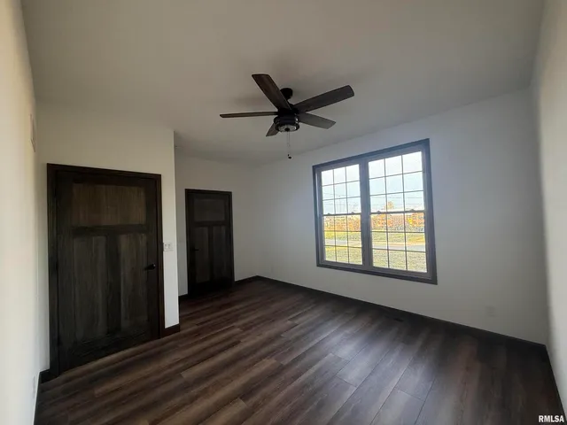 an empty room with wooden floor a ceiling fan and windows