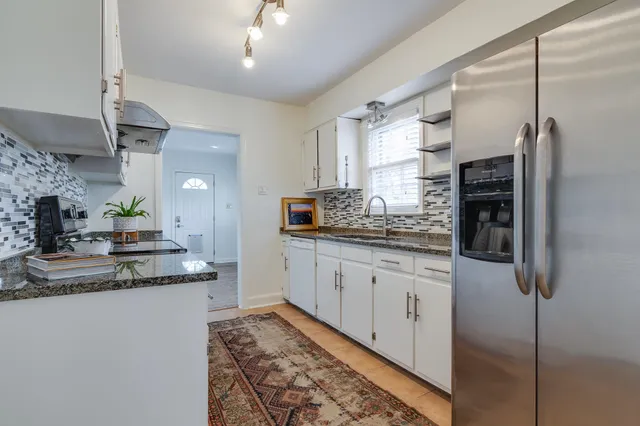 a kitchen with stainless steel appliances granite countertop a refrigerator a oven and white cabinets with wooden floor