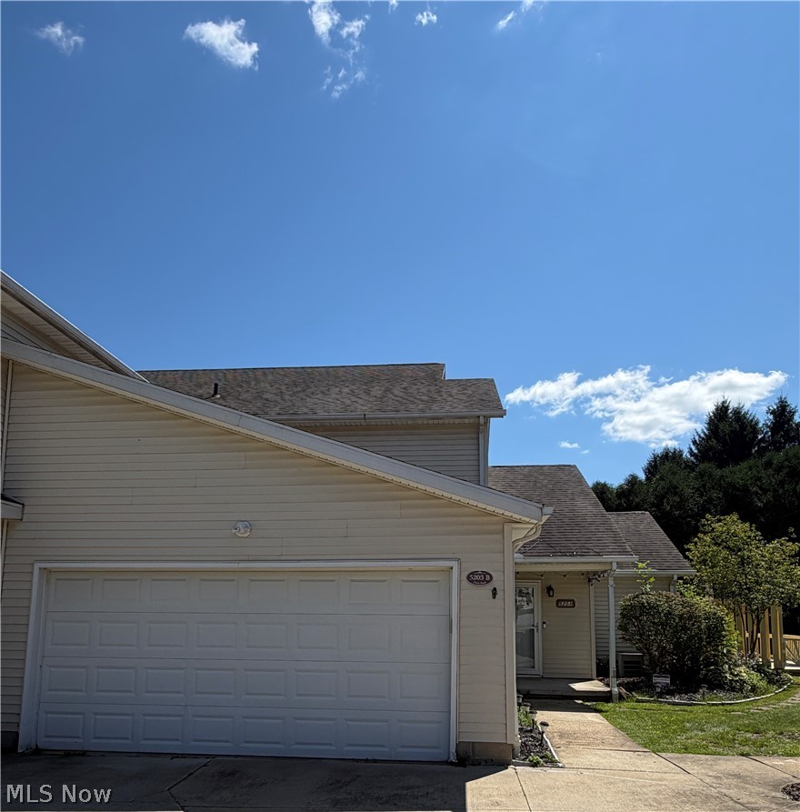 Charming ranch-style home featuring a spacious two-car garage with paneled doors, light-colored vinyl siding, and a pitched roof with architectural shingles