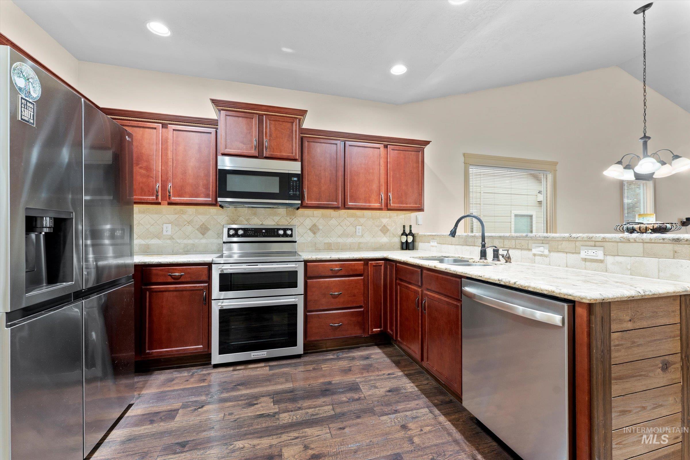 176 East Breinholt Street Meridian, ID 83646 - Photo 3 of 39 Kitchen featuring stainless steel appliances, a peninsula, dark wood finished floors, decorative light fixtures, and a chandelier