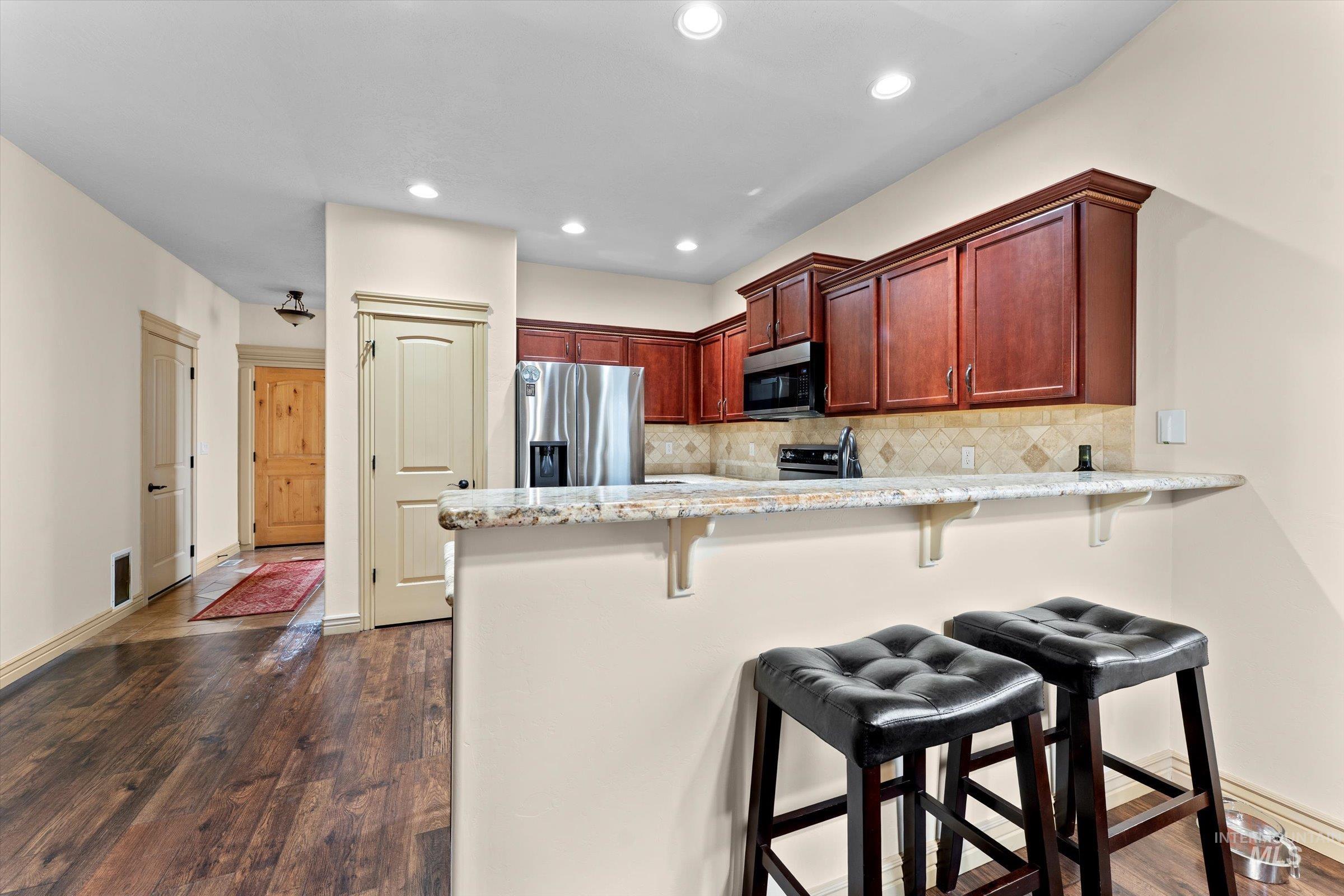 176 East Breinholt Street Meridian, ID 83646 - Photo 5 of 39 Kitchen with a peninsula, dark wood-type flooring, a breakfast bar, appliances with stainless steel finishes, and light stone countertops