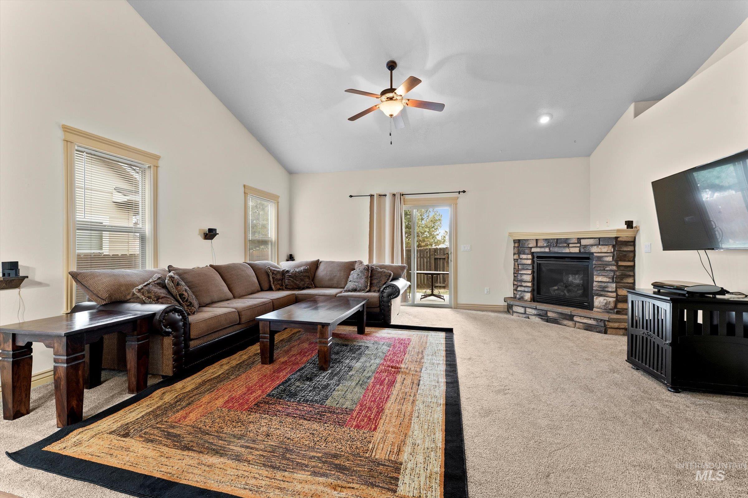 176 East Breinholt Street Meridian, ID 83646 - Photo 9 of 39 Living area featuring a stone fireplace, light carpet, lofted ceiling, and a ceiling fan