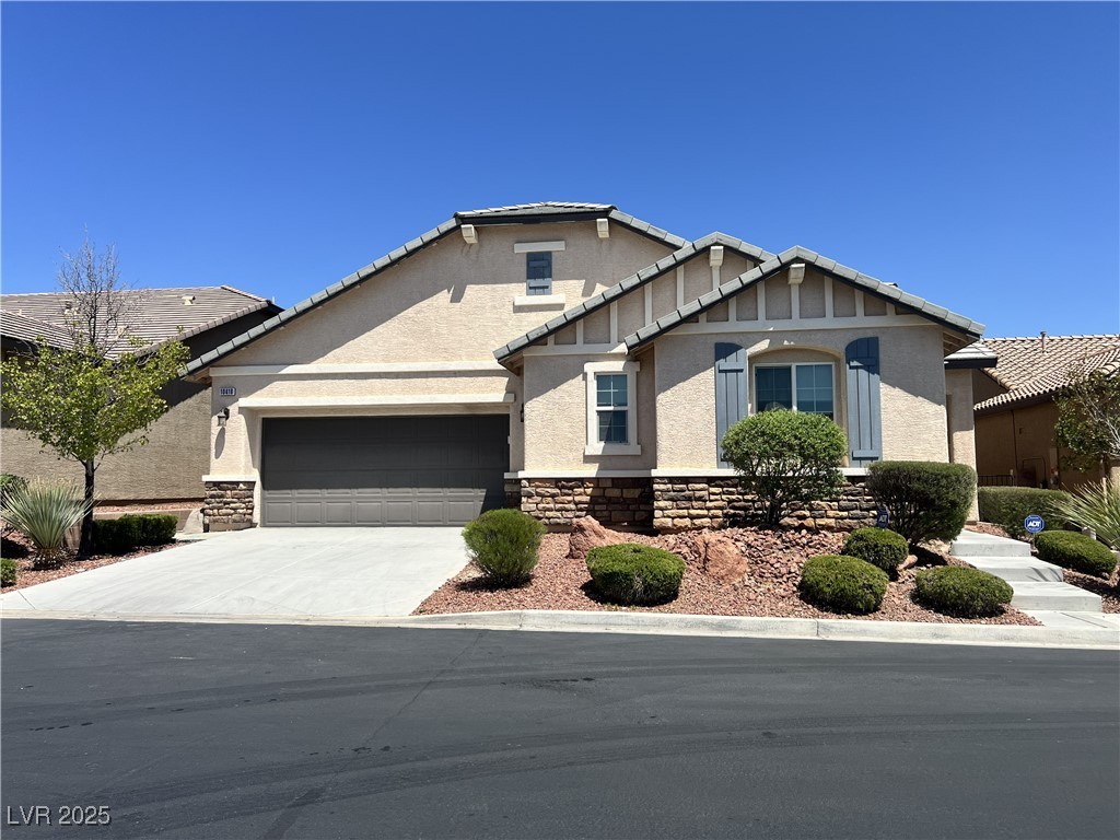 View of front of property featuring stone siding, driveway, stucco siding, and an attached garage