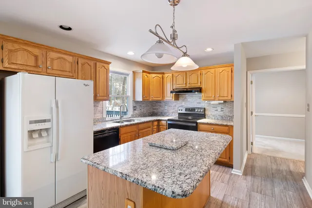 a kitchen with stainless steel appliances granite countertop a refrigerator a sink dishwasher a stove and white countertops with wooden floor