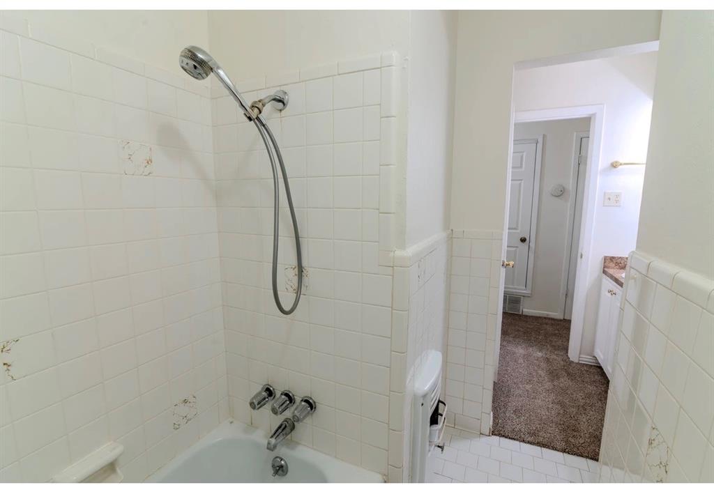 8017 Woodhue Road Dallas, TX 75228 - Photo 12 of 20 Bathroom featuring a showerhead with flexible hose, a built-in bathtub, and ceramic tile walls