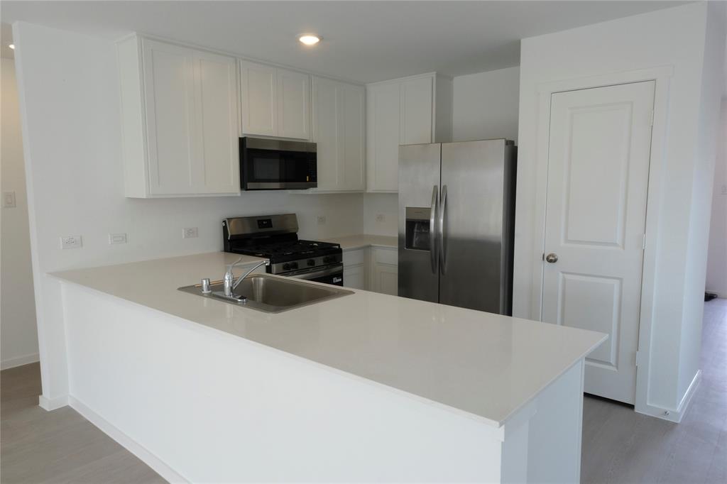 932 Calley Pear Trail Princeton, TX 75407 - Photo 7 of 16 a kitchen with stainless steel appliances a refrigerator a sink a stove a microwave and wooden cabinets