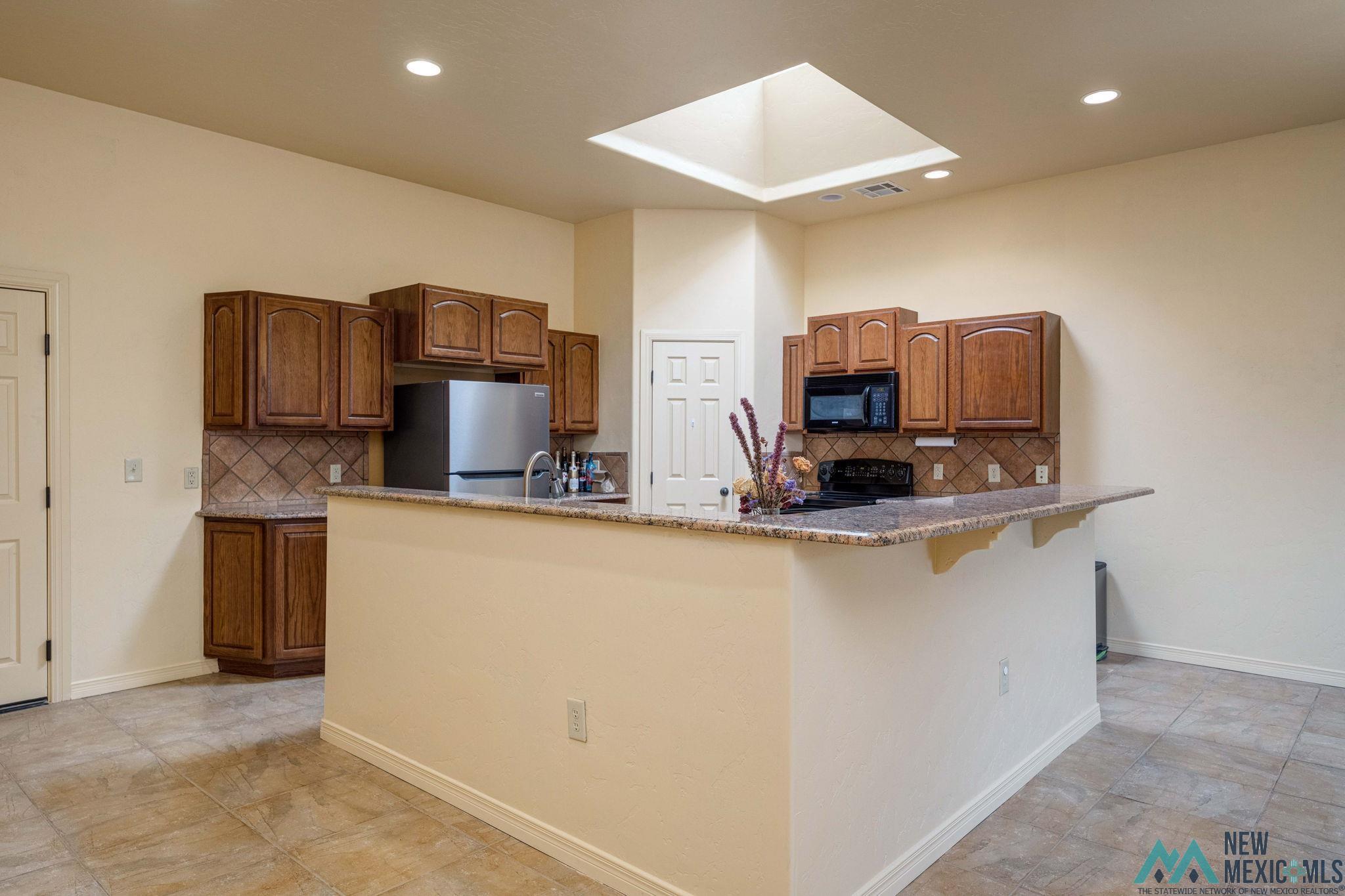 3884 Adriatic Road Las Cruces, NM 88012 - Photo 13 of 45 Kitchen featuring wood cabinetry, a granite-finish breakfast bar, tiled flooring, recessed lighting, and a skylight