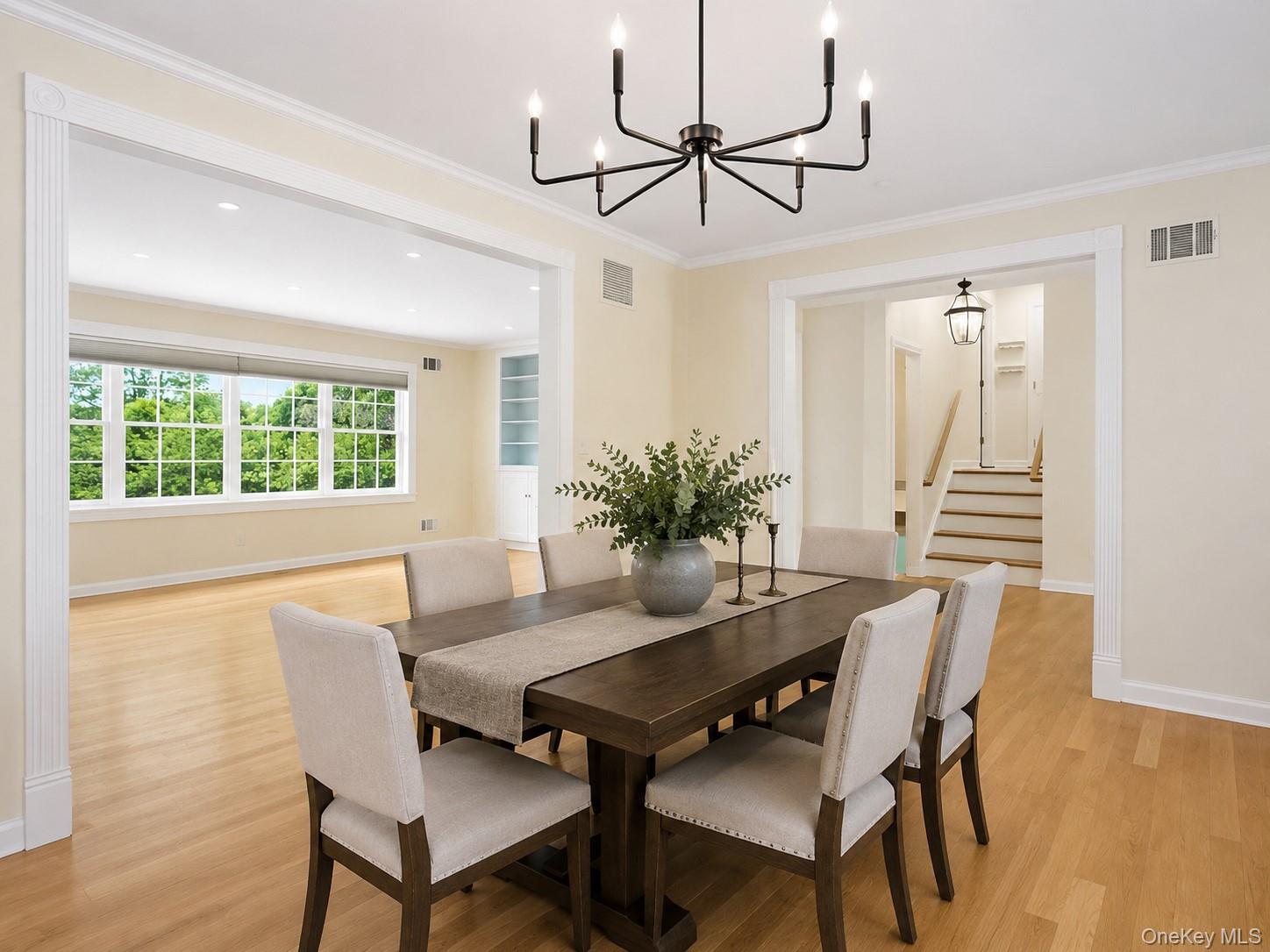 26 Century Ridge Road Purchase, NY 10577 - Photo 6 of 50 Dining area featuring a modern black chandelier, light hard wood flooring, and crown molding; open flow to the living room and kitchen (Table/ chairs Virtually Staged)