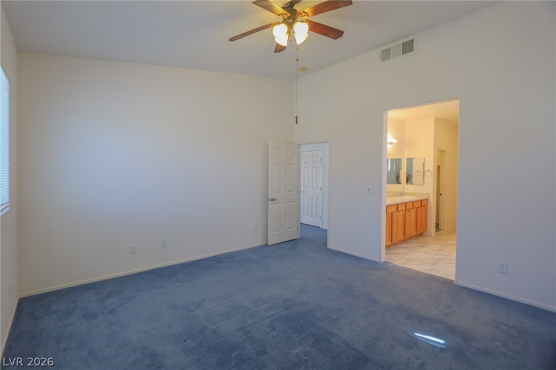 6472 Centennial Road Pahrump, NV 89048 - Photo 6 of 29 A spacious primary bedroom features soft blue carpeting and vaulted ceilings, connecting to a private bathroom.