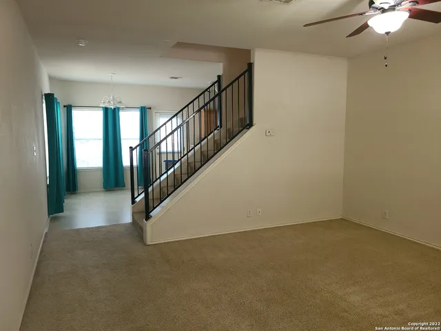 a view of an empty room with stairs and a chandelier fan