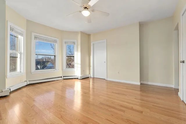 an empty room with wooden floor chandelier fan and windows