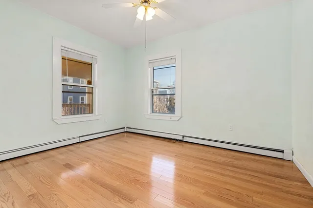 an empty room with wooden floor chandelier fan and windows