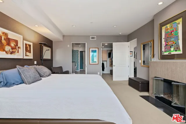 a spacious bedroom with a bed a painting on the wall and a flat screen tv