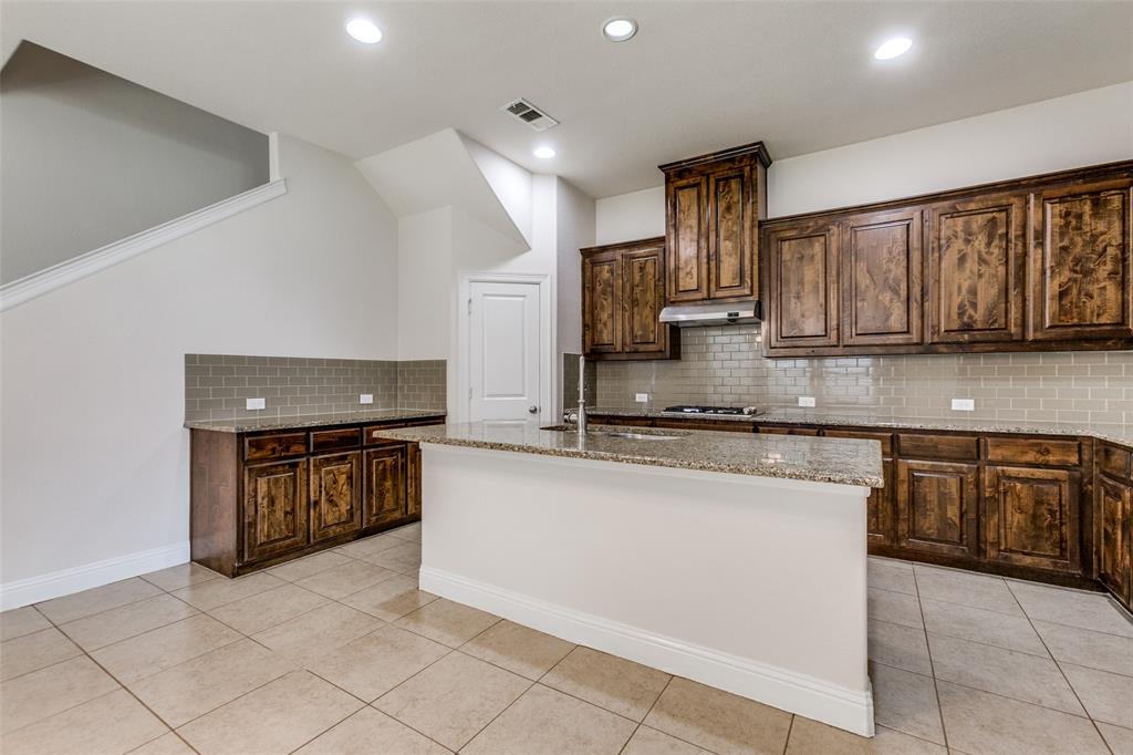 12618 Akenside Road Frisco, TX 75035 - Photo 10 of 31 Kitchen featuring a kitchen island with sink, decorative backsplash, light tile patterned floors, and light stone countertops
