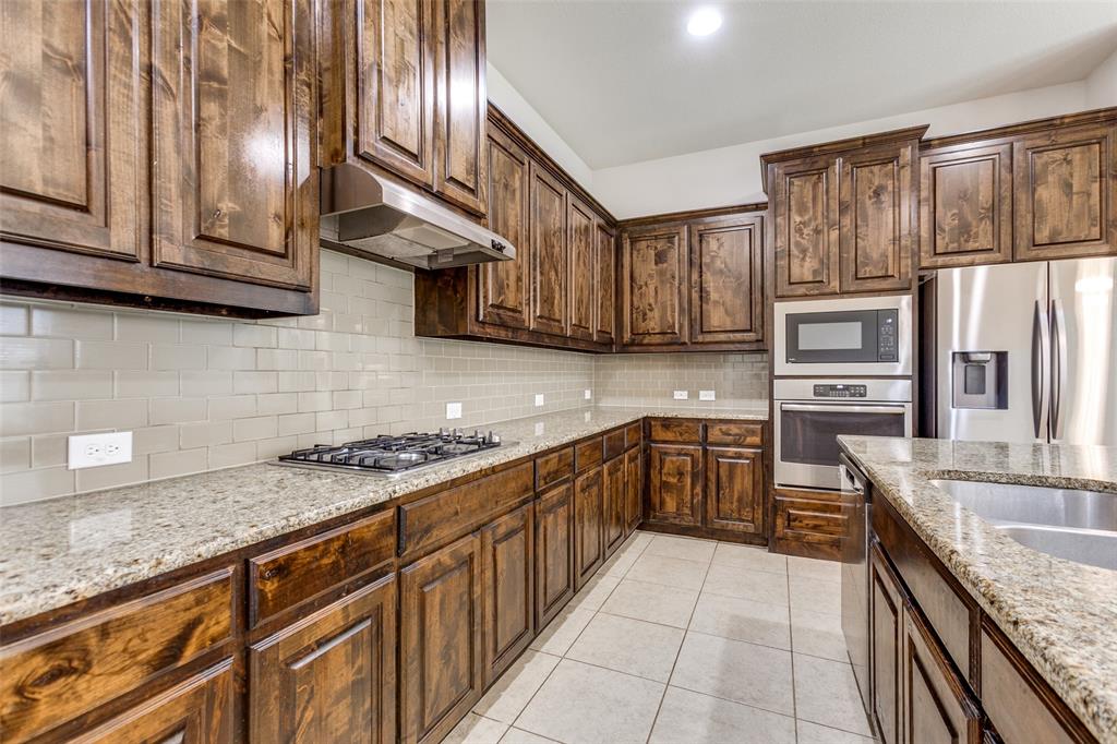 12618 Akenside Road Frisco, TX 75035 - Photo 12 of 31 Kitchen featuring light tile patterned floors, backsplash, light stone counters, and stainless steel appliances