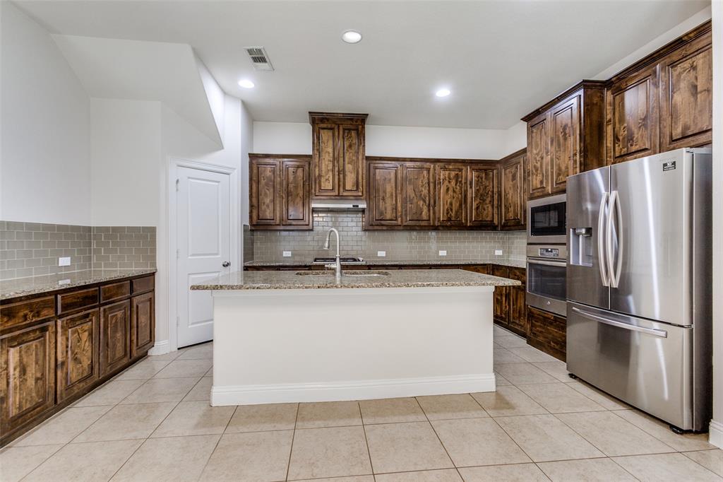 12618 Akenside Road Frisco, TX 75035 - Photo 7 of 31 Kitchen with appliances with stainless steel finishes, decorative backsplash, an island with sink, light stone countertops, and light tile patterned floors