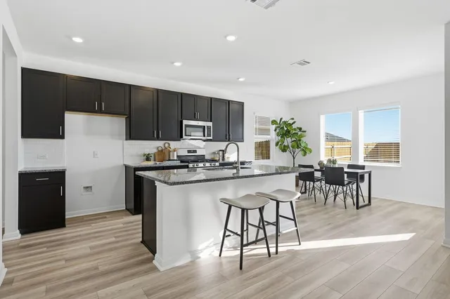 a kitchen with stainless steel appliances granite countertop a stove a refrigerator a sink a dining table and chairs with wooden floor