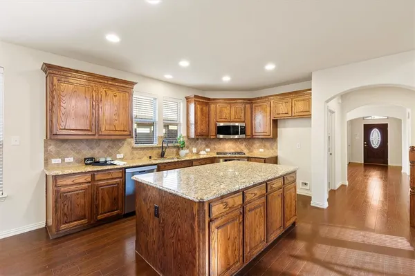 a kitchen with stainless steel appliances granite countertop a stove a sink dishwasher and a refrigerator with wooden floor