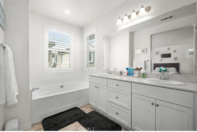 a bathroom with a double vanity sink a mirror a bathtub and next to a window