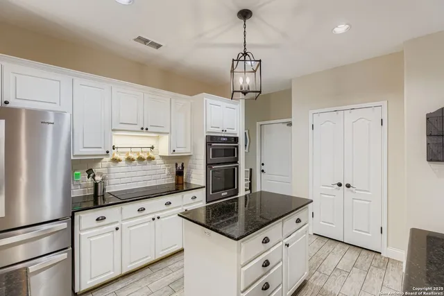 a kitchen with stainless steel appliances granite countertop a refrigerator a sink dishwasher a stove and white cabinets with wooden floor