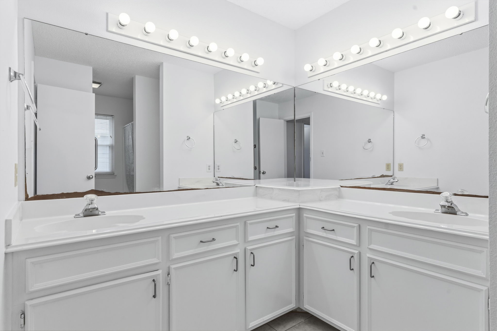 119 Sand Shoals Road Freeport, TX 77541 - Photo 21 of 34 Primary ensuite bath — L-shaped double-sink vanity with white cultured marble counters, two Hollywood-style vanity bars, oversized mirrors, deep cabinet storage, and tile flooring.
