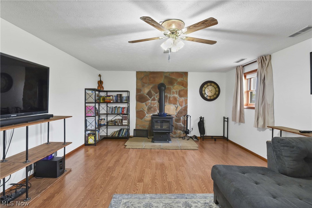 9550 Spencer Road Homerville, OH 44235 - Photo 20 of 50 Spacious room featuring a stone-clad wall, built-in wood-burning stove with a stone hearth, wood-finish flooring, and a ceiling fan