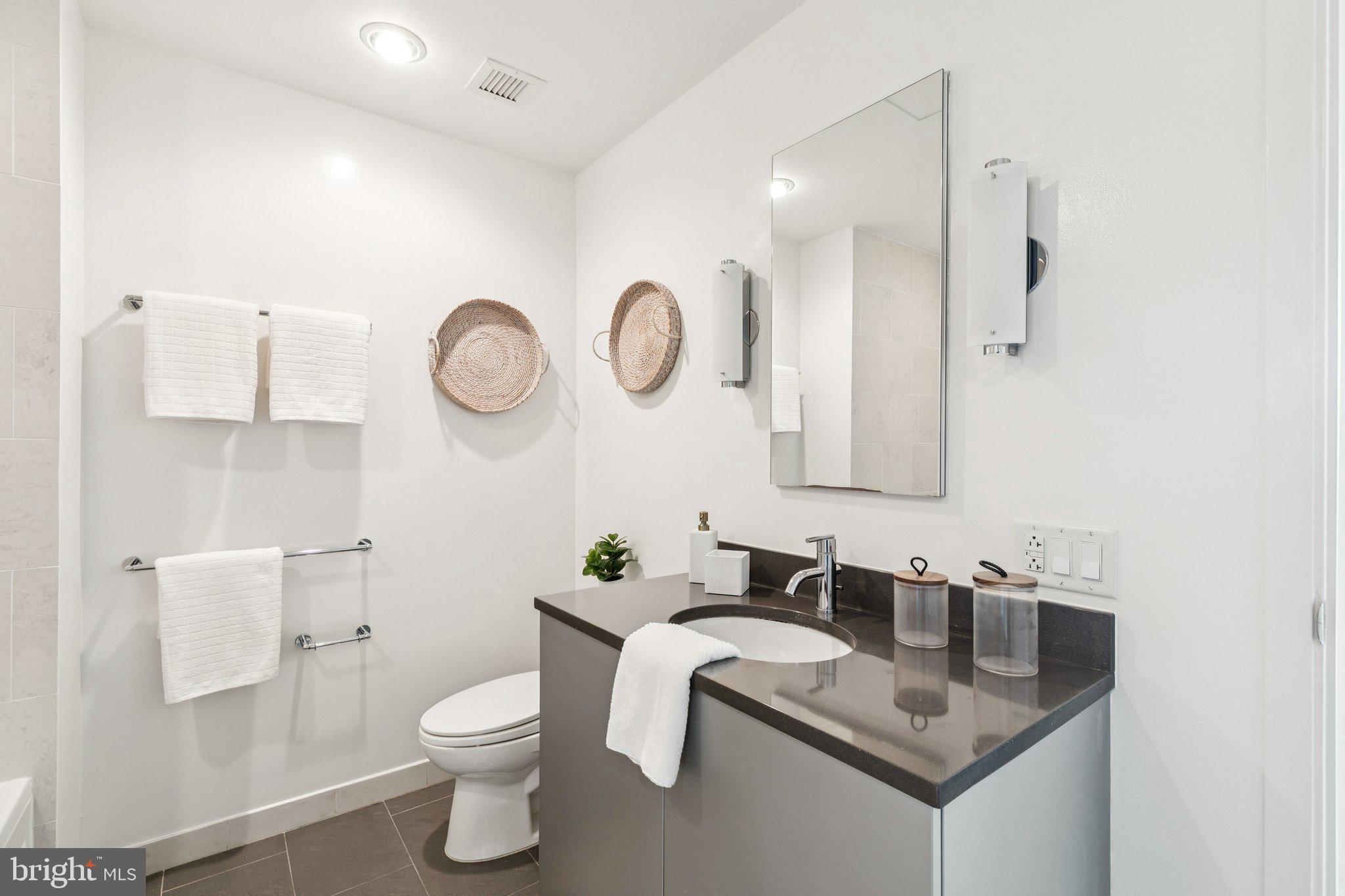 2101 Market Street, Unit 905 Philadelphia, PA 19103 - Photo 17 of 30 a bathroom with a granite countertop sink a toilet and a mirror