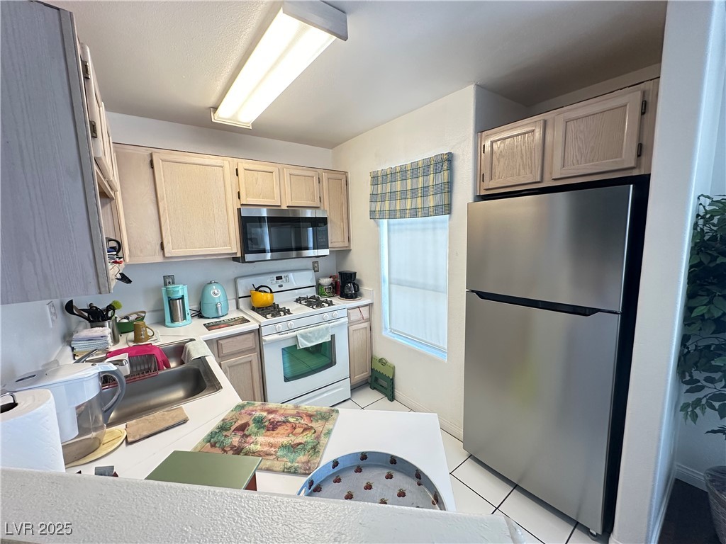 698 South Racetrack Road, Unit 322 Henderson, NV 89015 - Photo 16 of 39 Kitchen featuring light brown cabinets, light countertops, a sink, light tile patterned floors, and stainless steel appliances