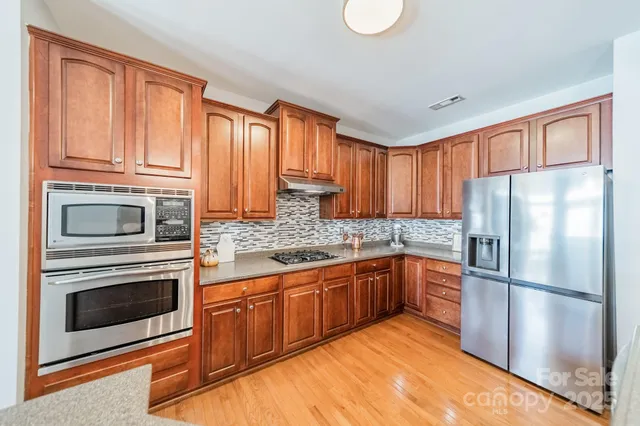 a kitchen with stainless steel appliances granite countertop a refrigerator a stove top oven a sink and dishwasher with wooden floor