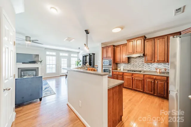 a kitchen with stainless steel appliances granite countertop wooden cabinets a refrigerator a stove a sink and dishwasher with wooden floor