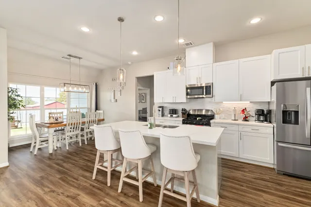 a kitchen with stainless steel appliances a dining table chairs refrigerator and sink