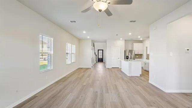 a view of an empty room with wooden floor and a kitchen