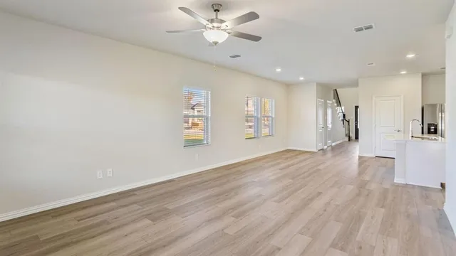 a view of an empty room with wooden floor and a ceiling fan