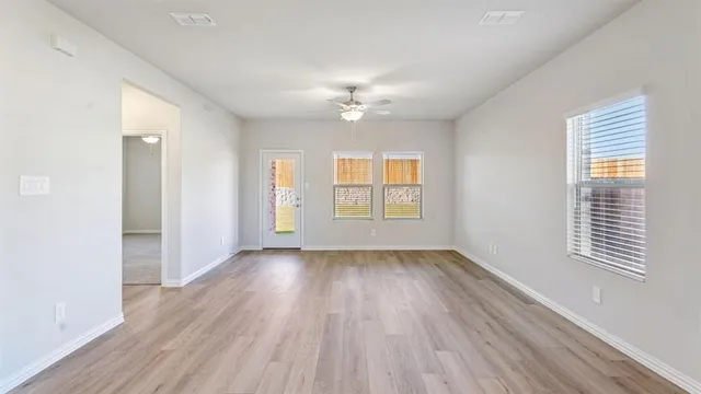 an empty room with wooden floor ceiling fan and windows