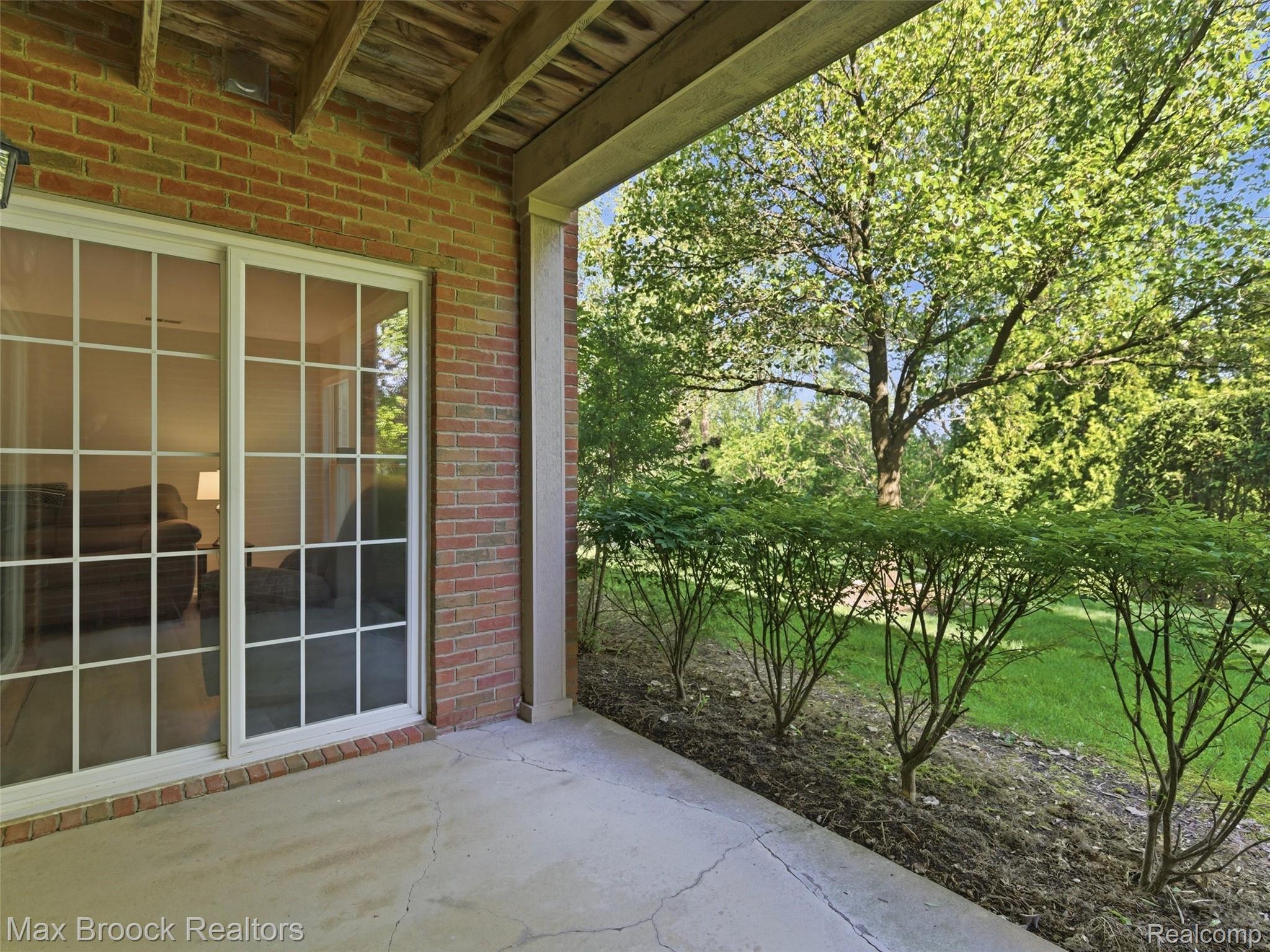 3562 Tremonte Circle Rochester, MI 48306 - Photo 24 of 33 Brick exterior with a covered concrete patio, featuring a sliding glass door with grid patterns, and a lush green lawn bordered by mature trees