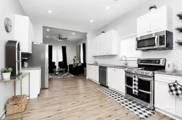 a kitchen with stainless steel appliances kitchen island granite countertop a refrigerator oven a sink dishwasher and white cabinets with wooden floor