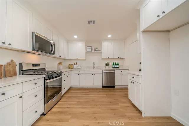 a kitchen with stainless steel appliances granite countertop white cabinets a sink a stove a refrigerator and white cabinets