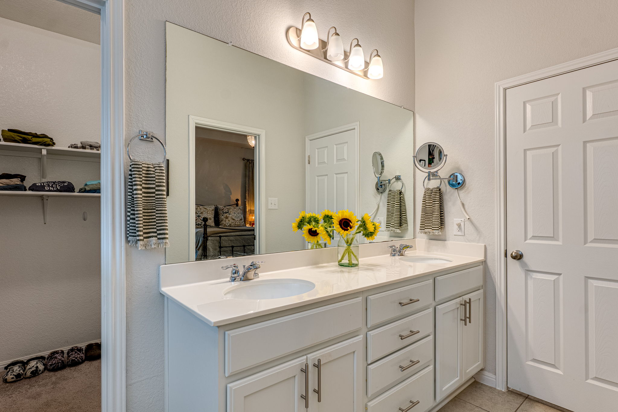 1009 Goldilocks Lane Manchaca, TX 78652 - Photo 21 of 40 Two sinks set into a light-toned countertop, featuring white cabinetry with brushed nickel hardware, a large wall-mounted mirror, a four-light fixture, and a paneled door is for the water closet.