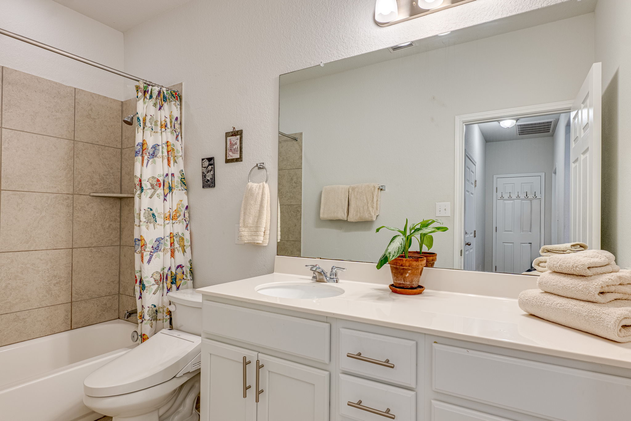 1009 Goldilocks Lane Manchaca, TX 78652 - Photo 27 of 40 Bathroom featuring a white vanity with built-in sink, expansive mirror, brushed nickel fixtures, and a shower-over-tub combination with large format tiled surround.