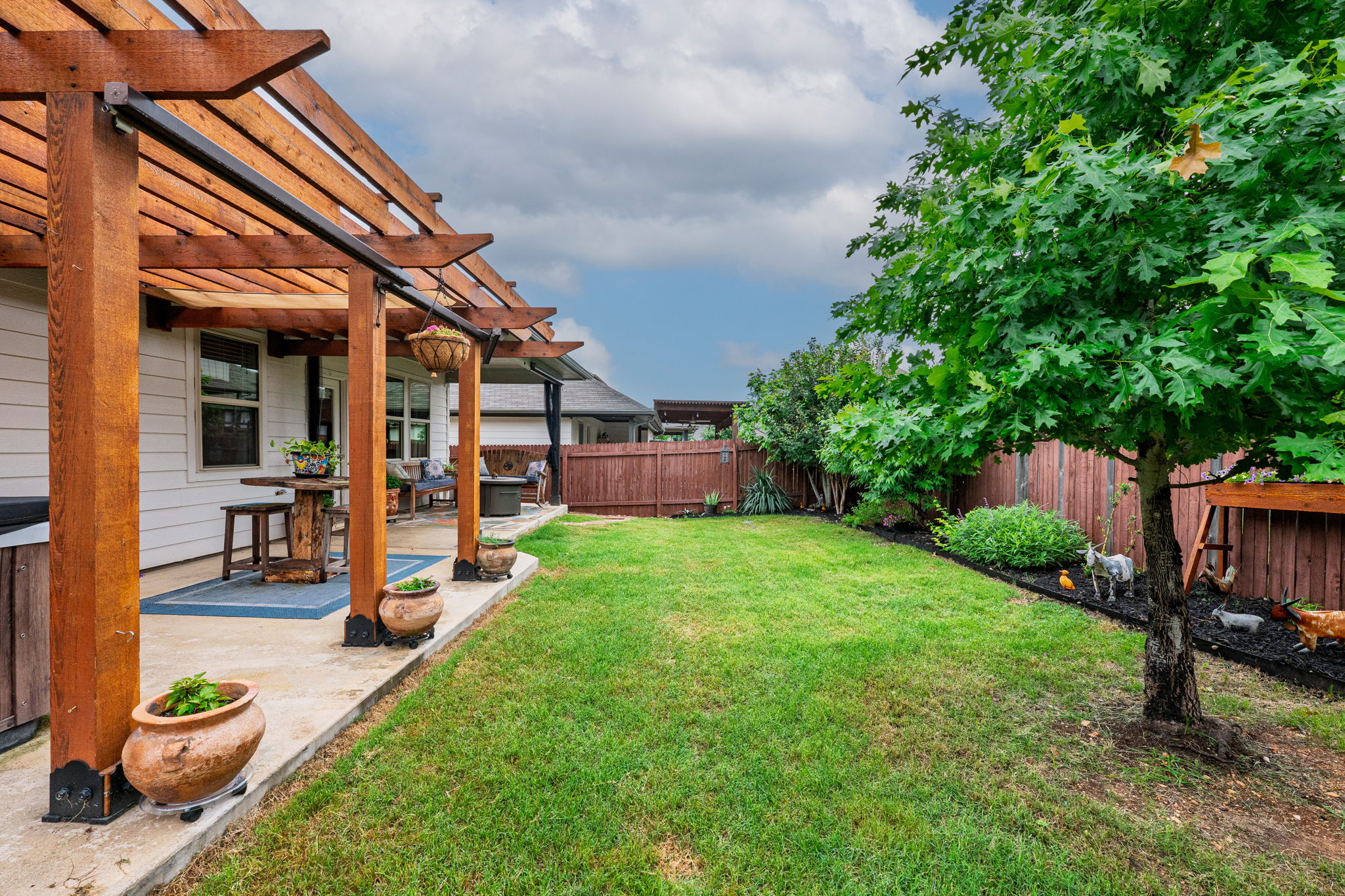 1009 Goldilocks Lane Manchaca, TX 78652 - Photo 31 of 40 Expansive backyard featuring a concrete patio, a wooden pergola, a privacy fence, trees, shrubs, and flowers.