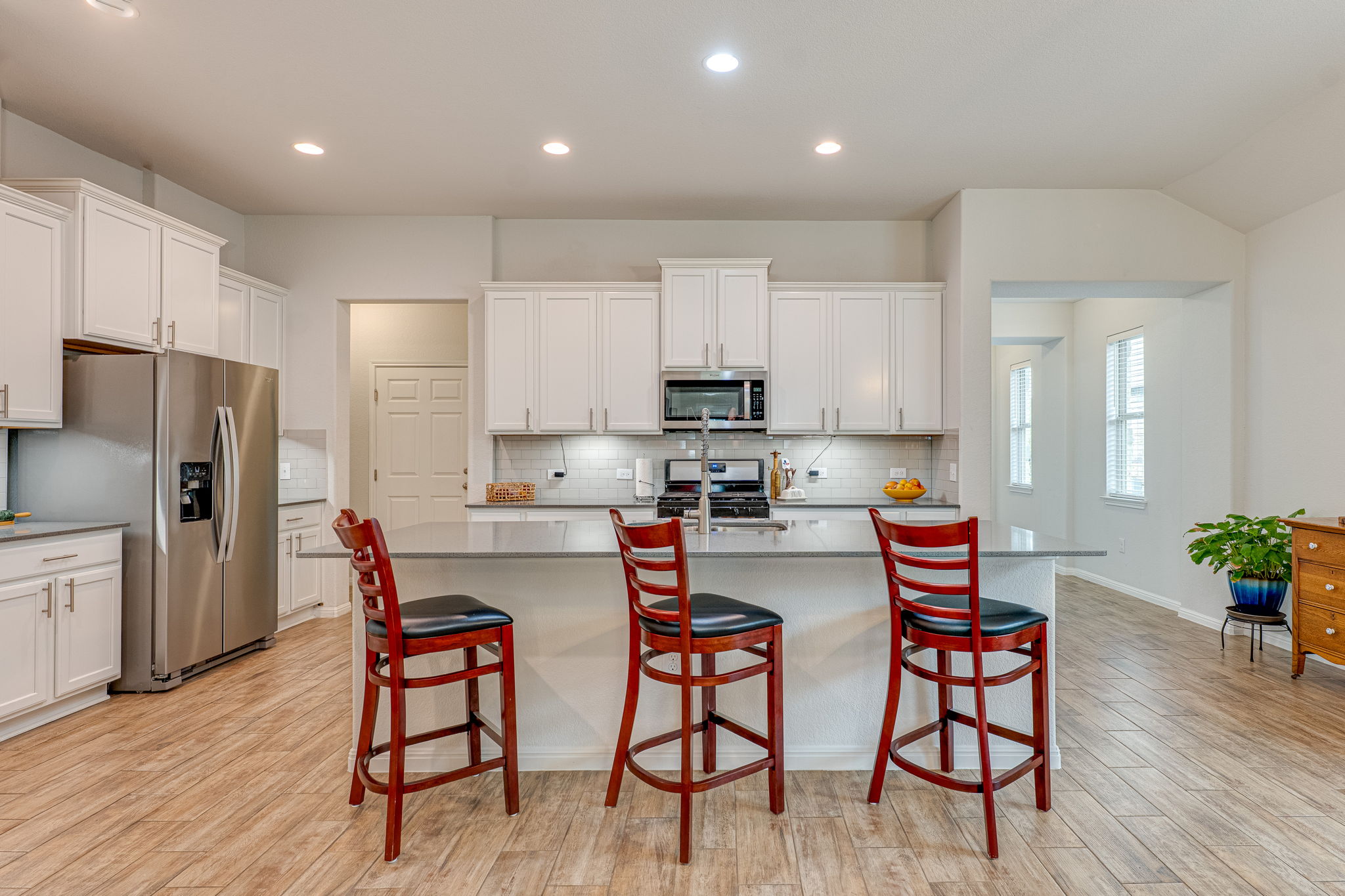 1009 Goldilocks Lane Manchaca, TX 78652 - Photo 4 of 40 Modern kitchen featuring 42" white cabinetry, stainless steel appliances, a large center island with a quartz countertop, wood-look tile flooring, and recessed lighting.