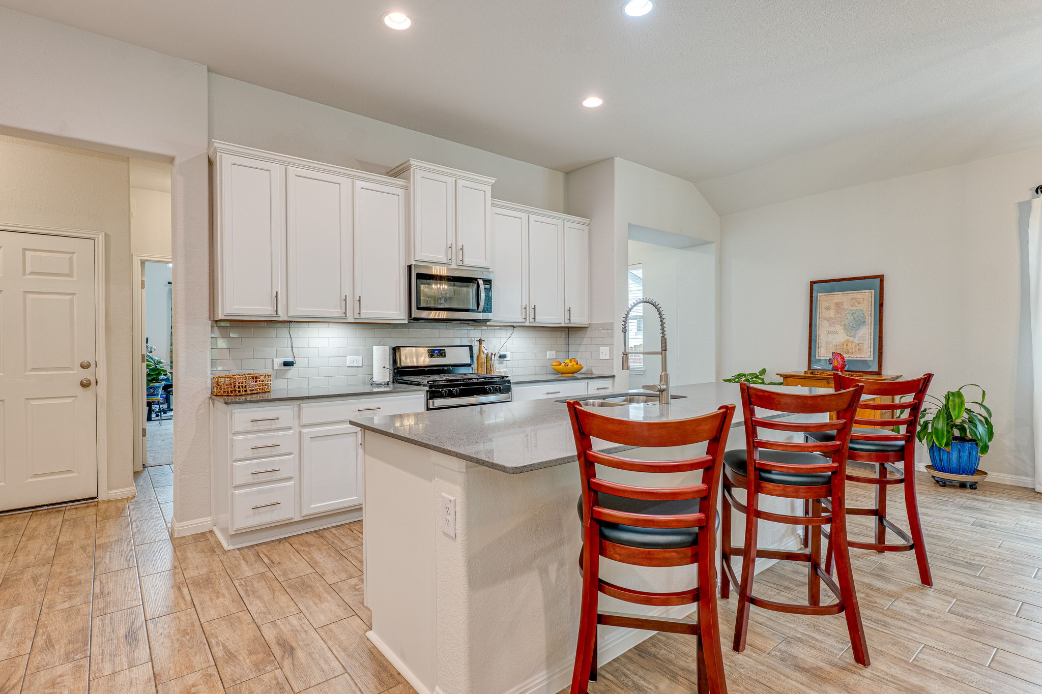 1009 Goldilocks Lane Manchaca, TX 78652 - Photo 5 of 40 Modern kitchen featuring 42" white cabinetry, stainless steel appliances, a large center island with a quartz countertop, wood-look tile flooring, and recessed lighting.