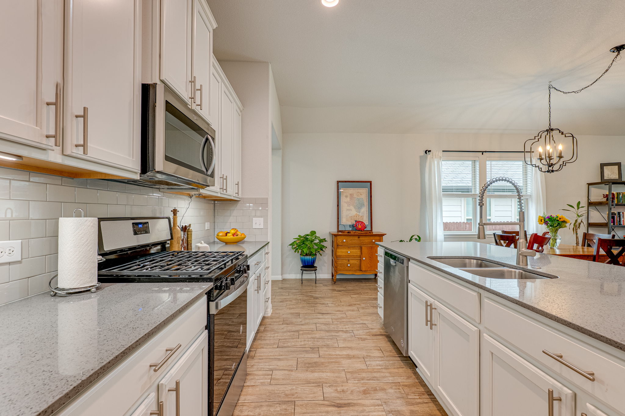 1009 Goldilocks Lane Manchaca, TX 78652 - Photo 6 of 40 Modern kitchen featuring 42" white cabinetry, stainless steel appliances, a large center island with a quartz countertop, wood-look tile flooring, and recessed lighting.