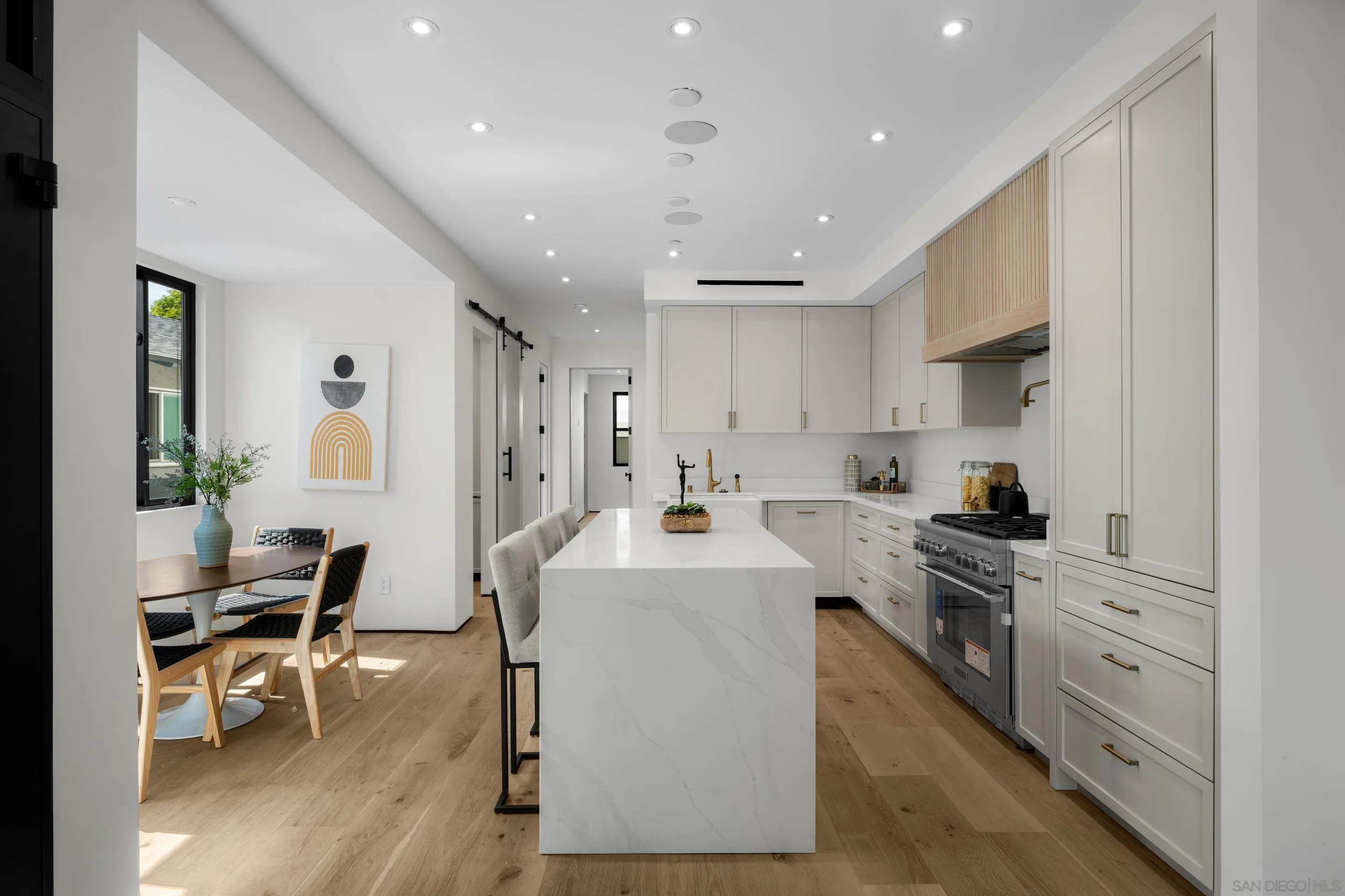 242 Playa Del Norte Street La Jolla, CA 92037 - Photo 12 of 32 a kitchen with white cabinets a sink stove and chairs with wooden floor