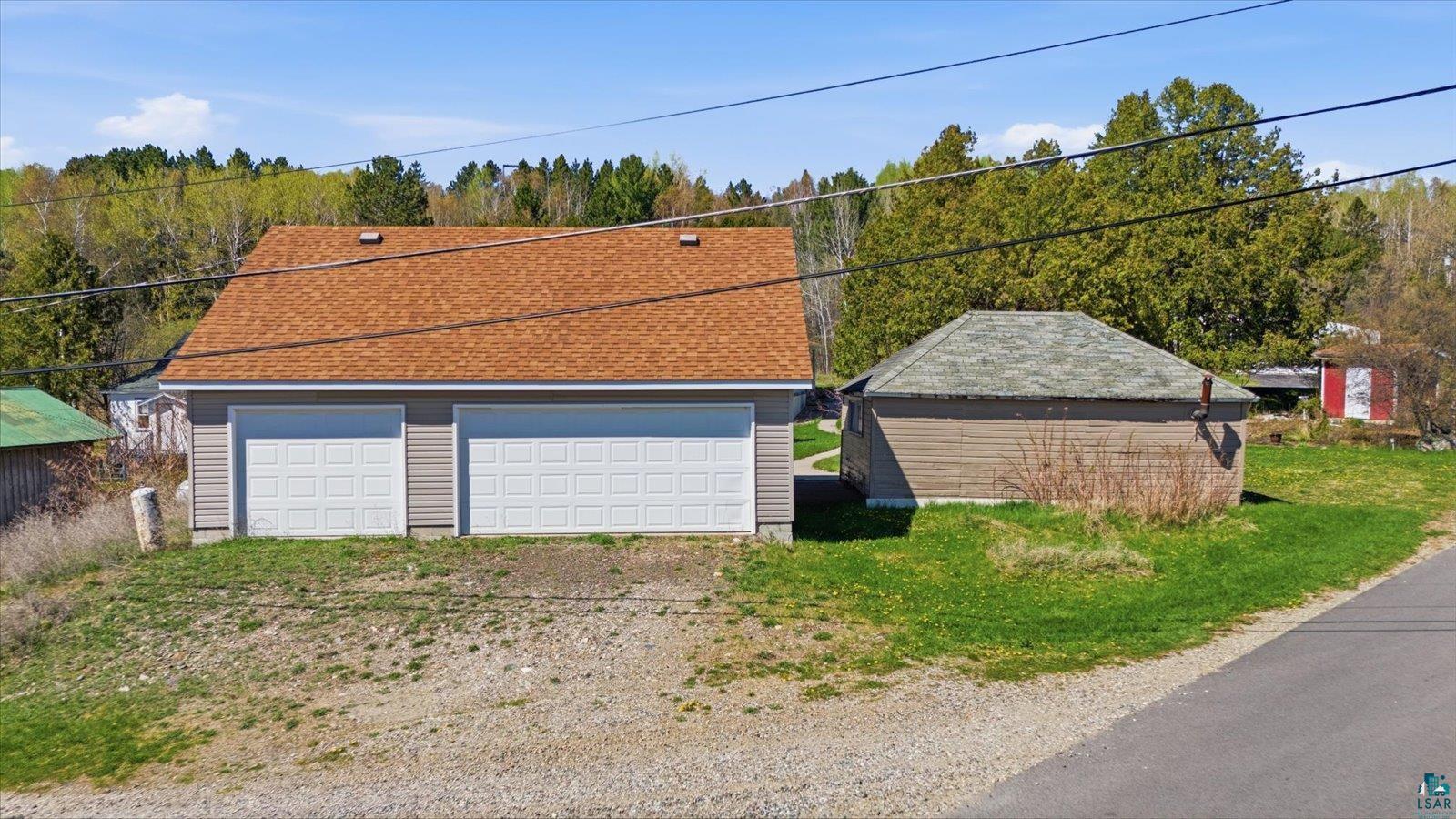 50 Main Street Soudan, MN 55782 - Photo 28 of 31 Two-car garage with tan horizontal siding and a brown shingle roof, complemented by a smaller, detached outbuilding featuring horizontal siding and a green roof