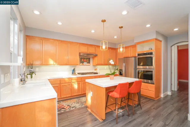 a kitchen with stainless steel appliances granite countertop a sink a stove a refrigerator and island with wooden floor